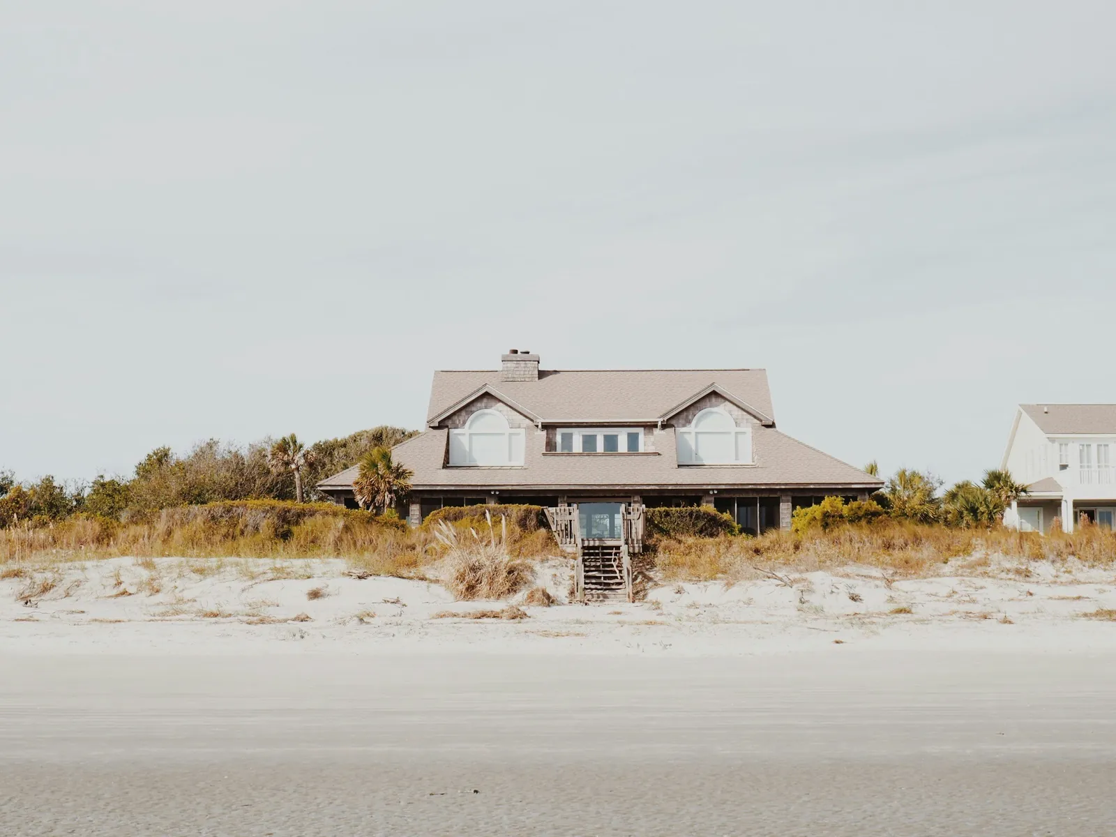 Coastal house behind dunes and vegetation near the beach.