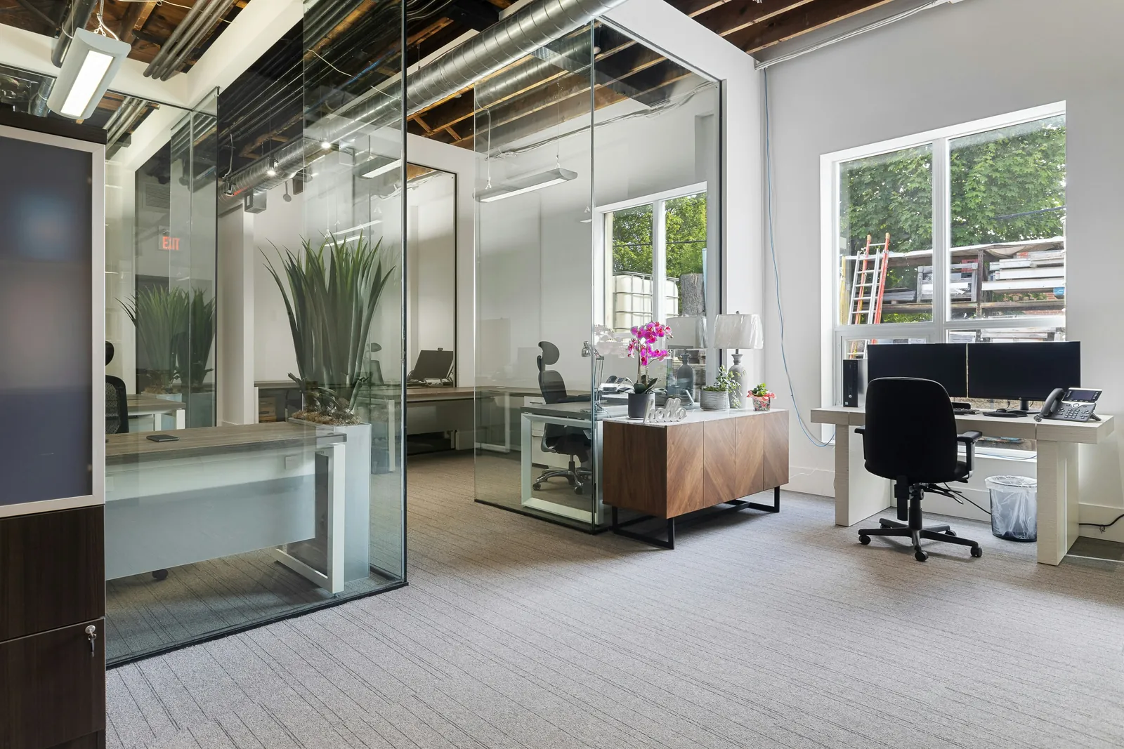 Modern office interior with gray painted walls, glass partitions, workstations, and exposed ceiling.