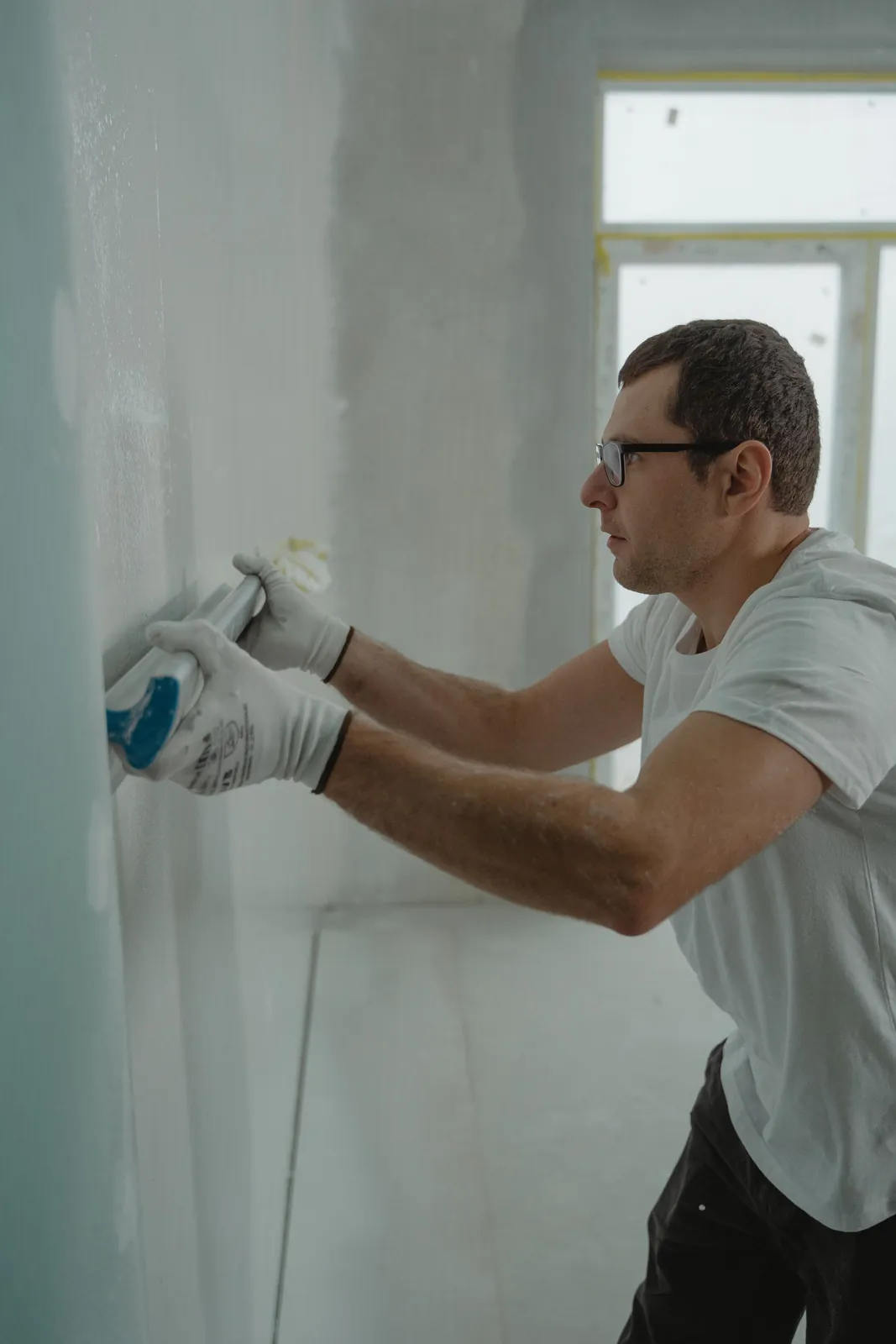Worker applying drywall compound to an interior wall before painting.