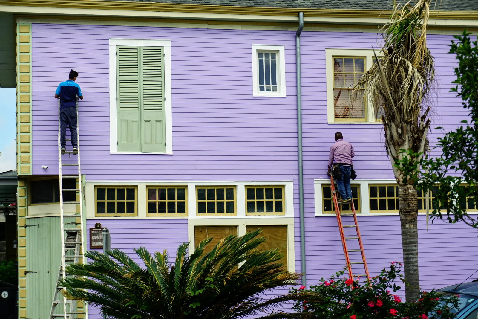 Two painters working from ladders on the siding of a coastal-style house.