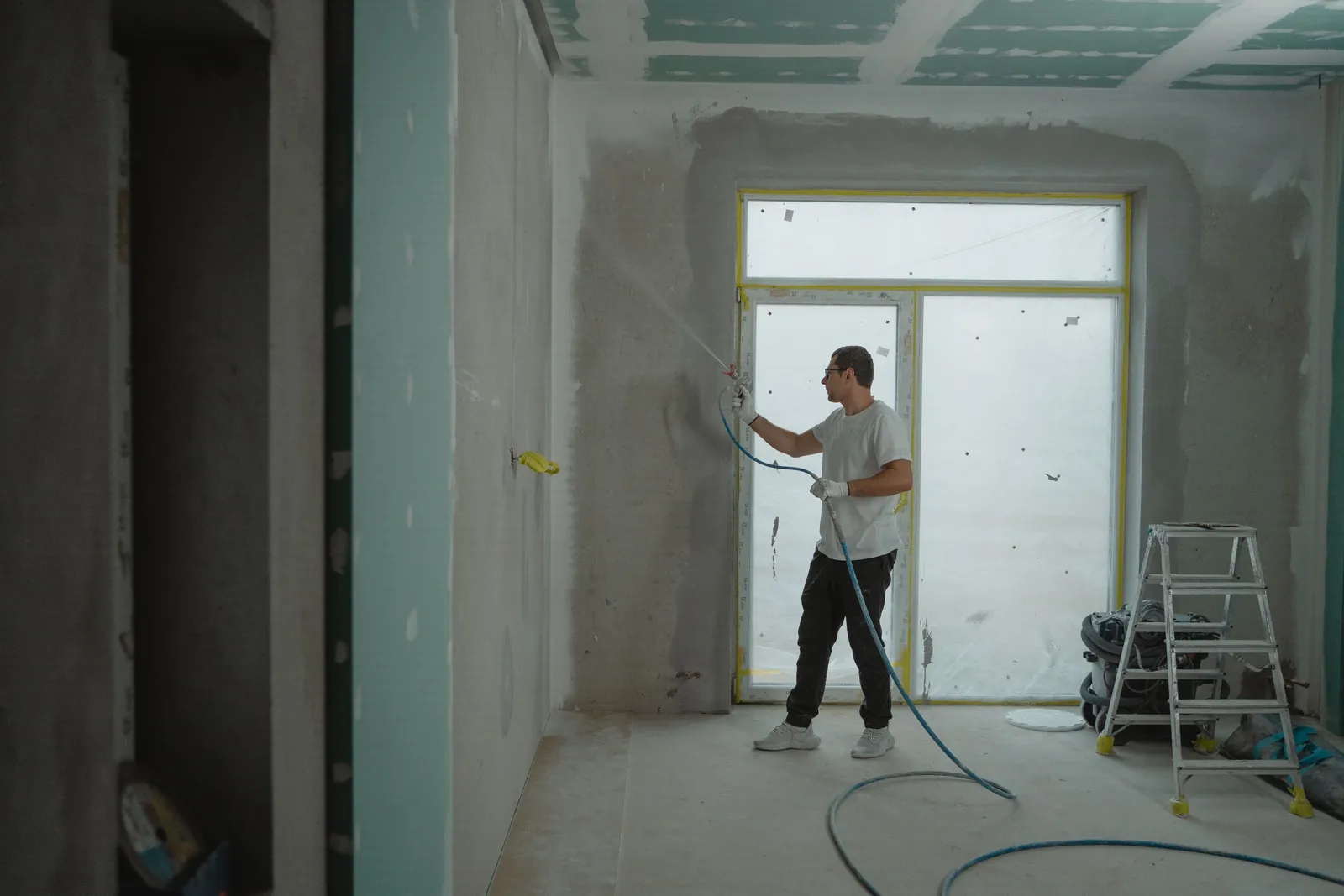 Professional painter spray-applying coating in a masked interior renovation space.