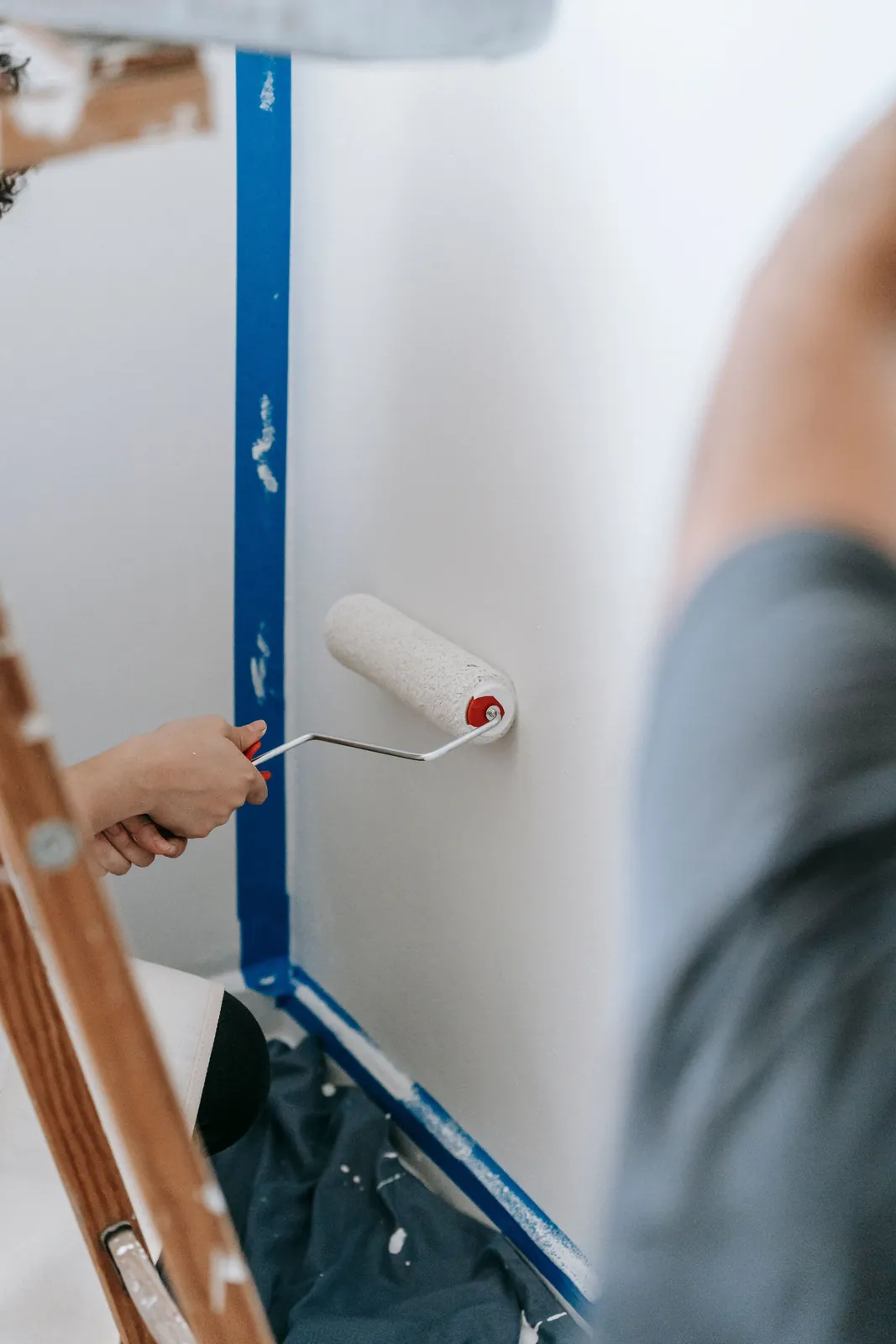 Small paint roller applying white paint beside blue painter's tape.
