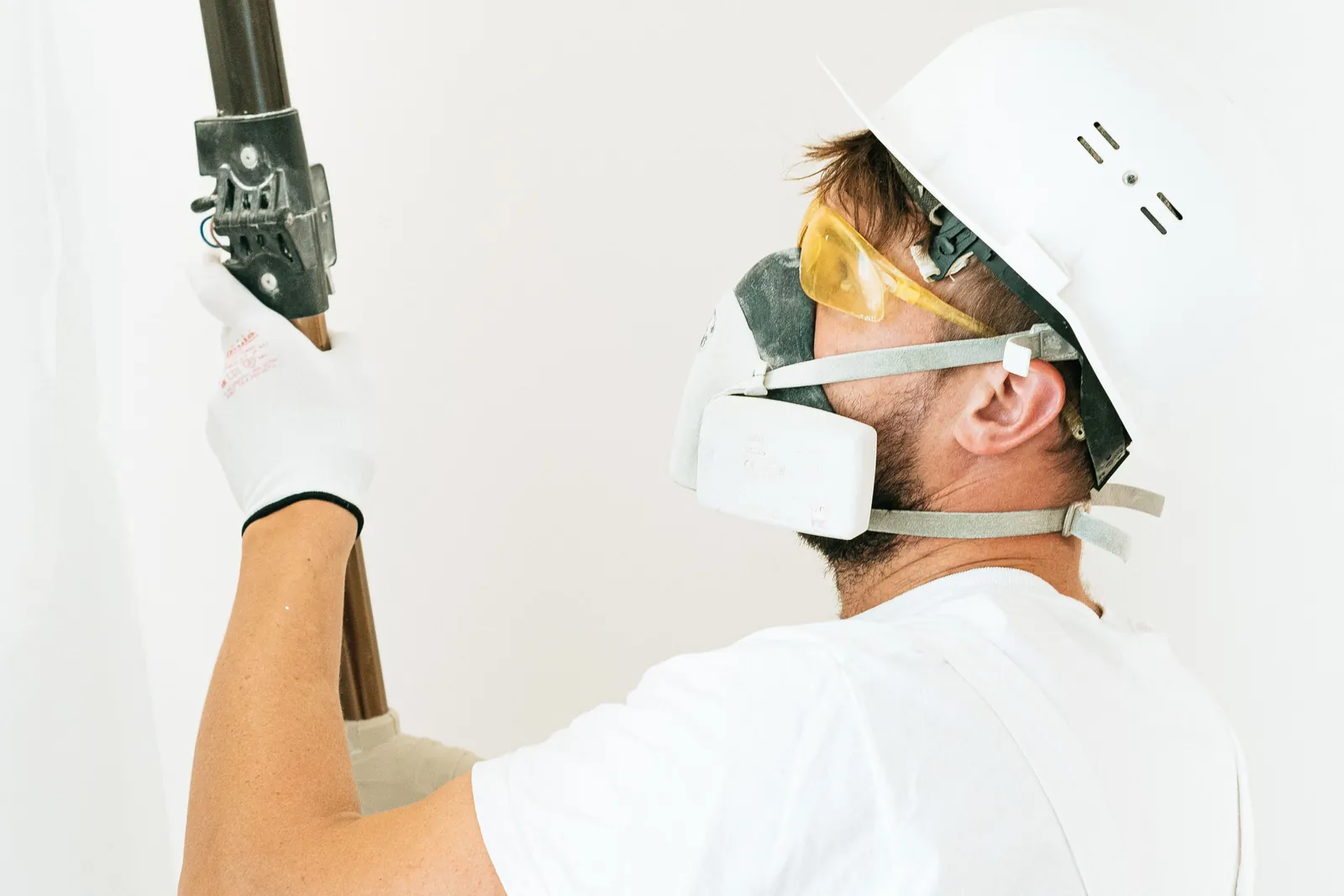 Painter wearing protective eyewear, respirator, gloves, and hard hat during surface preparation.