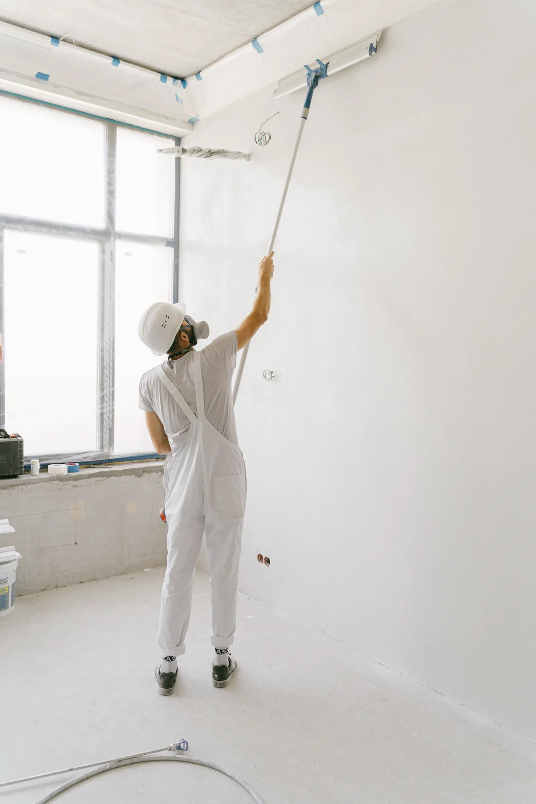 Professional painter rolling white paint on a tall interior wall.