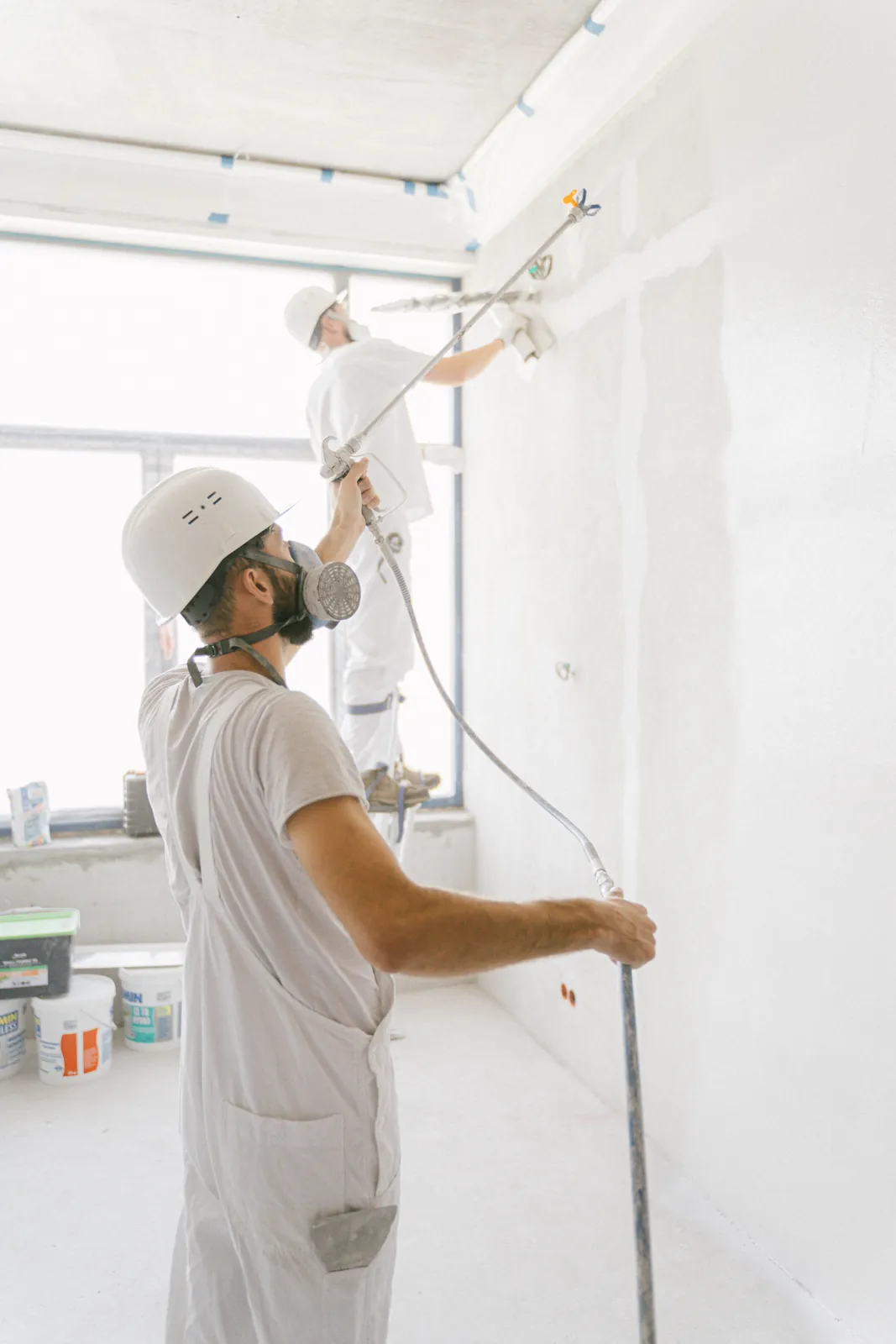 Two painters using spray equipment on interior walls during a renovation.