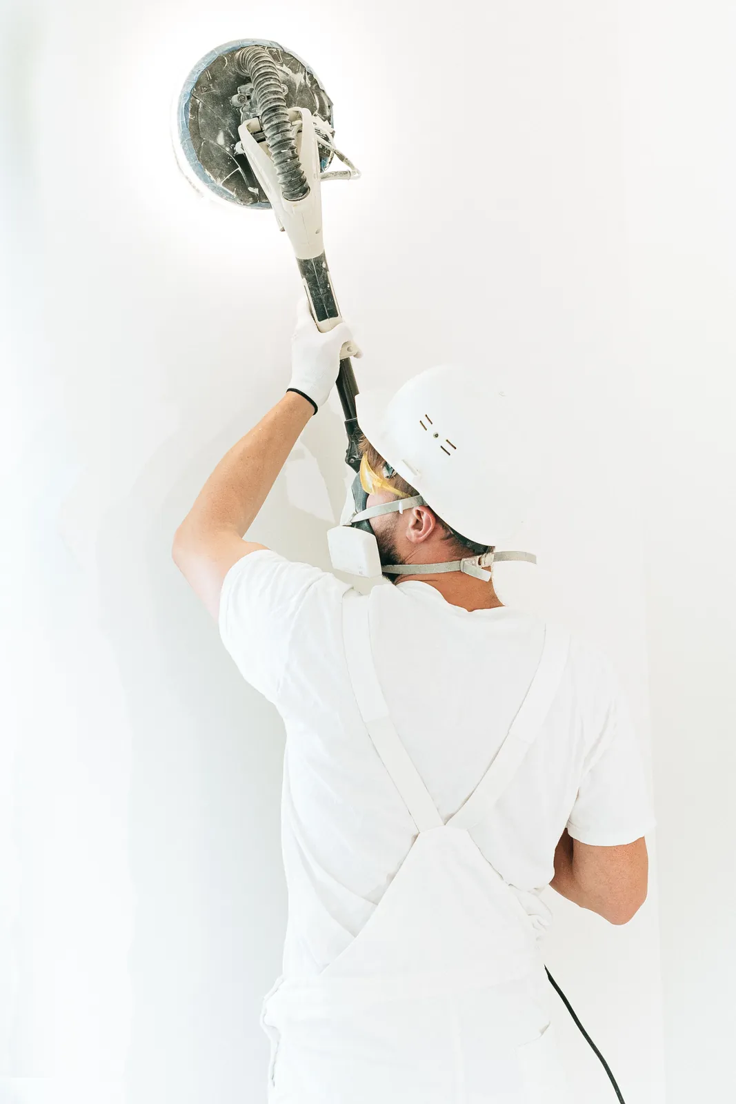 Painter sanding an interior wall with dust-control equipment before coating.